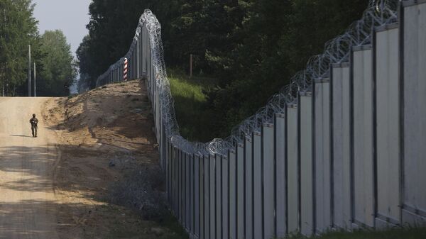 Польский пограничник идет вдоль металлического забора на границе Польши и Белоруссии