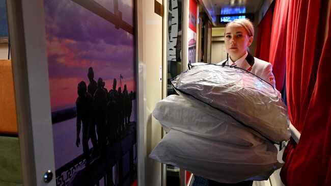 Проводница несет комплекты постельного белья пассажирам