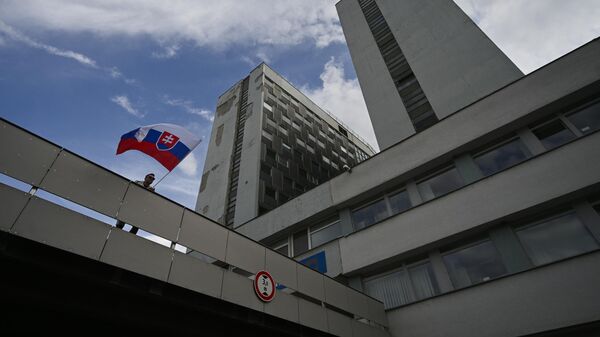 Мужчина с флагом Словакии у здания университетской больницы имени Ф. Д. Рузвельта, где проходит лечение раненый премьер-министр Роберт Фицо, в Банска-Бистрице