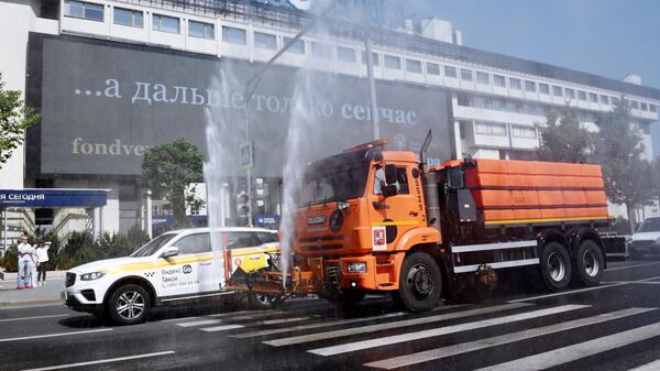Автомобиль коммунальных служб поливает проезжую часть дороги на Зубовском бульваре в Москве