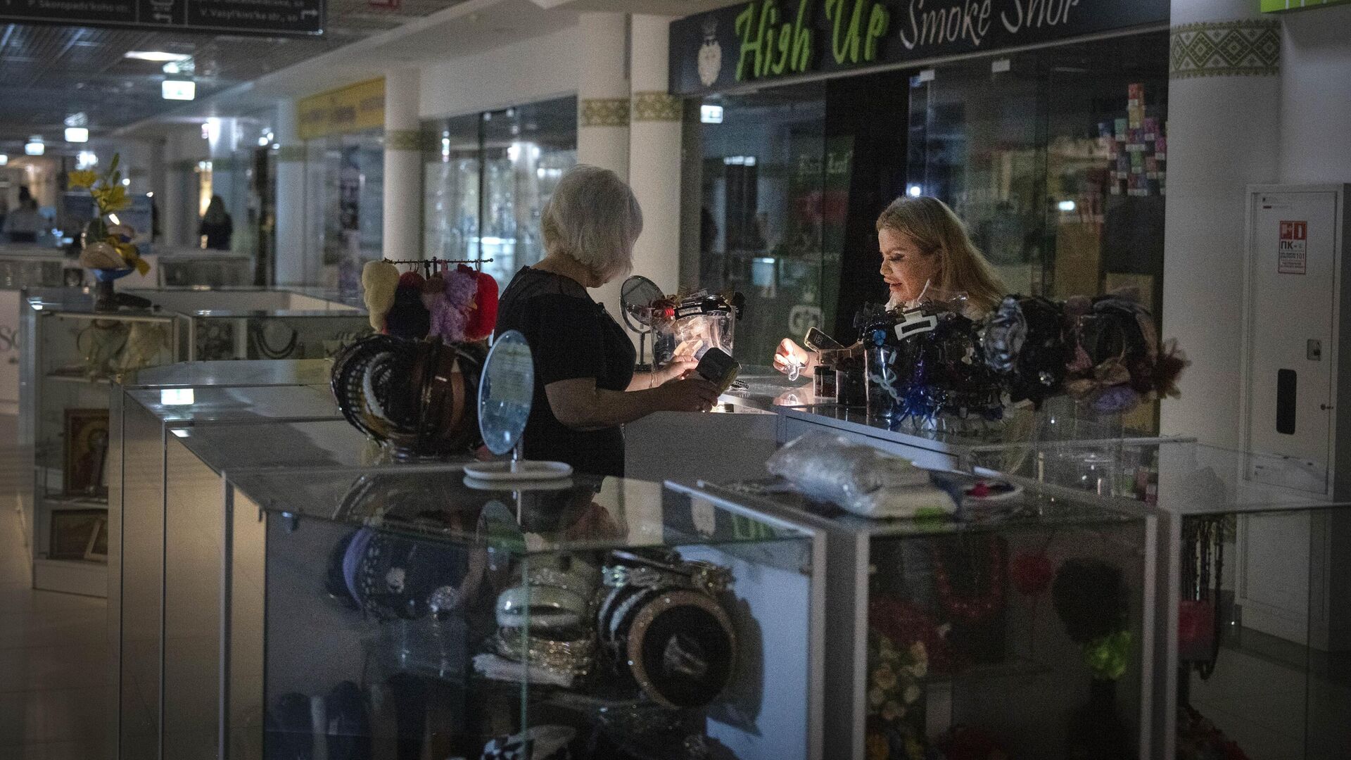 Продавец показывает товары покупателю при помощи фонарика в подземном торговом центре во время отключения электроэнергии в Киеве - РИА Новости, 1920, 21.06.2024