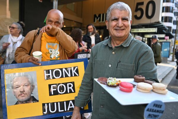 Мужчина раздает сладости сторонникам Джулиана Ассанжа перед зданием посольства США в Сиднее 