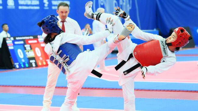 Тогжан Казнабек (Казахстан) и Анара Ганыева (Киргизия) в полуфинальном поединке в весовой категории до 55 кг в соревнованиях по тхэквондо среди женщин на международных спортивных играх Дети Азии в Якутске.