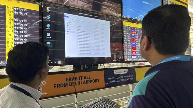 Сотрудники аэропорта пытаются перезагрузить экран с информацией о рейсах в международном аэропорту имени Индиры Ганди в Нью-Дели