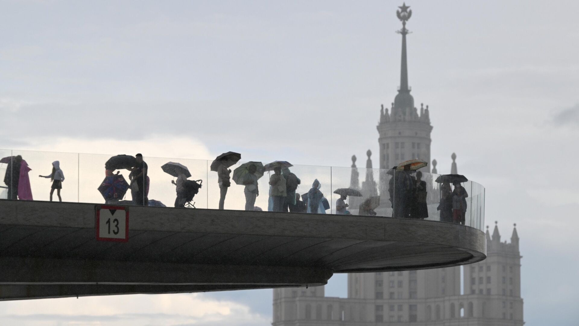 Люди на Парящем мосту во время дождя в природно-ландшафтном парке Зарядье в Москве0