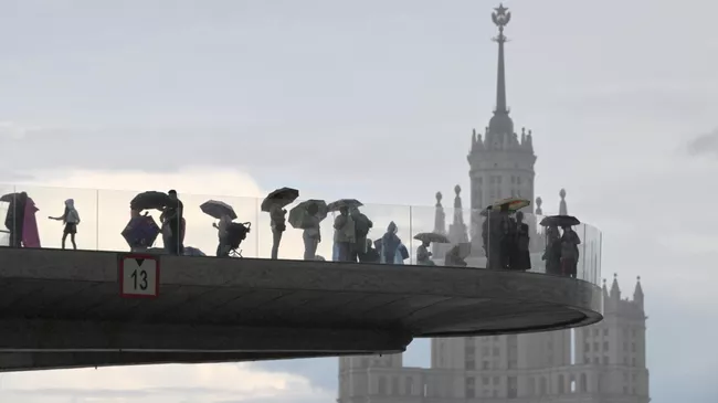 Люди на Парящем мосту во время дождя в природно-ландшафтном парке Зарядье в Москве