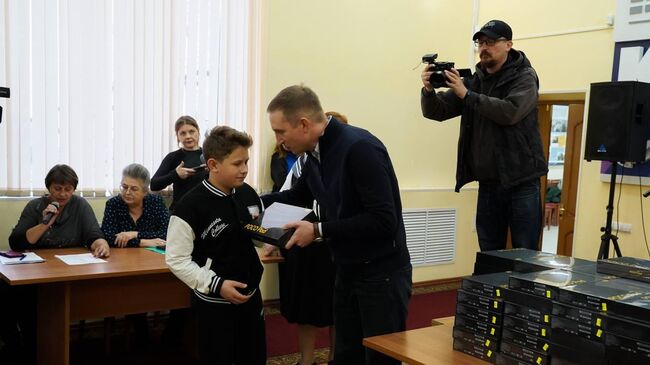 Начальник отдела министерства социального развития, опеки и попечительства Иркутской области Алексей Дмитриев передает планшет школьнику из Курской области