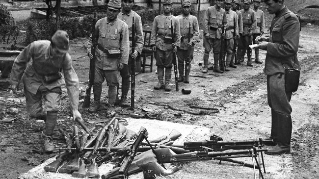 Солдаты капитулирующей Квантунской армии Японии сдают оружие советскому офицеру. На земле сложены винтовки Арисака (Тип 99) и пулеметы Намбу (Тип 11).