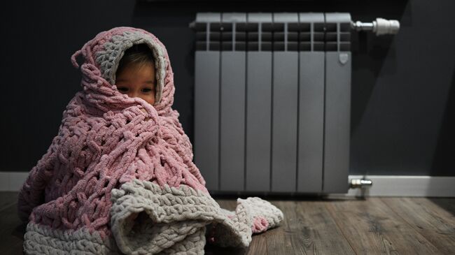 Девочка в пледе сидит возле батареи