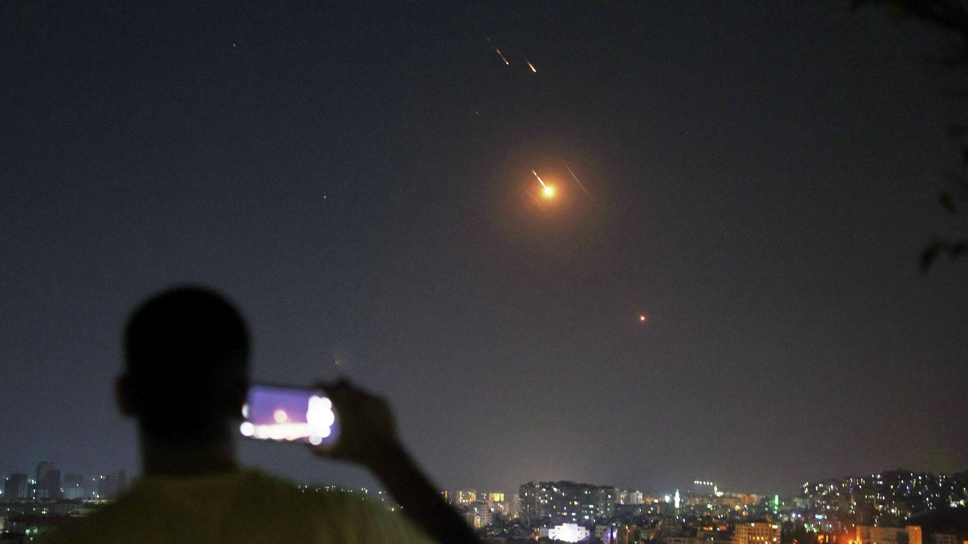 Мужчина снимает на мобильный телефон, как ракеты, выпущенные из Ирана в сторону Израиля, пролетают над Дамаском, Сирия - РИА Новости, 1920, 18.06.2025