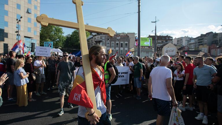 Молодой человек несет деревянный крест на плече на площади Славия в Белграде во время акции протеста Молодой человек несет деревянный крест на плече на площади Славия в Белграде во время акции протеста