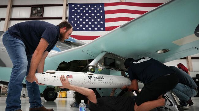 Сотрудники Venus Aerospace вешают дрон на крыло учебного самолета в Хьюстоне, США