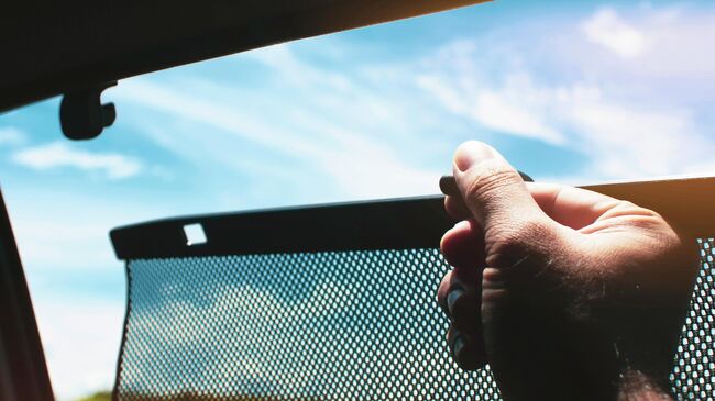 Водитель поднимает шторки на боковых окнах автомобиля