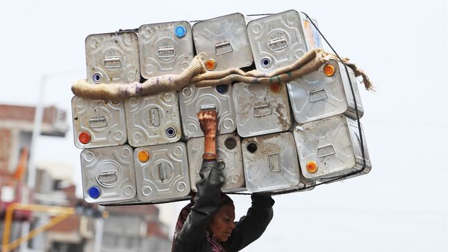 Женщина несет на голове пустые канистры из-под моторного масла в Ахмадабаде, Индия