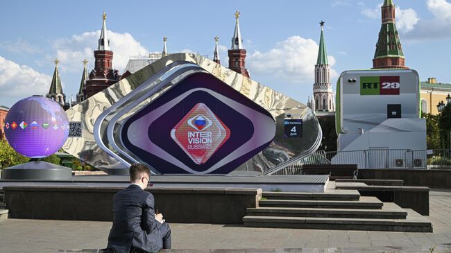 Мужчина перед сценой с символикой международного музыкального конкурса Интервидение на Манежной площади в Москве