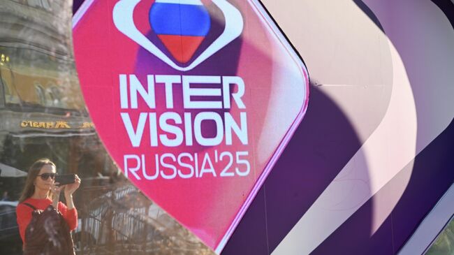 Девушка рядом с банером международного музыкального конкурса Интервидение на Манежной площади в Москве. Конкурс пройдёт 20 сентября 2025 года, на него заявлены участники из 23 стран