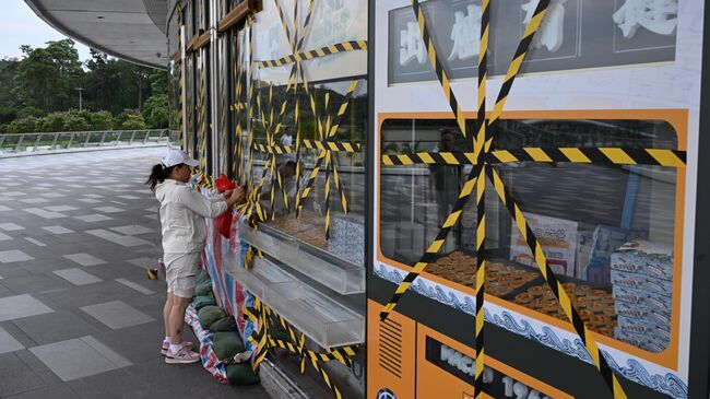 Сотрудница магазина заклеивает окна перед приходом супертайфуна Рагаса в провинции Гуандун, Китай