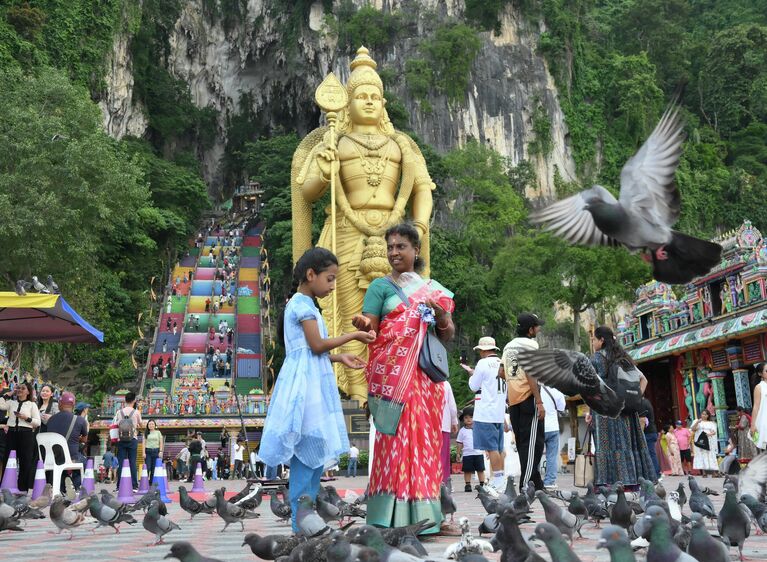 Туристы кормят птиц у пещер Бату в Куала-Лумпуре. На втором плане – статуя бога Муругана Туристы кормят птиц у пещер Бату в Куала-Лумпуре. На втором плане – статуя бога Муругана