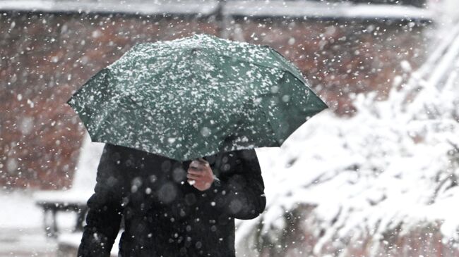 Прохожий с зонтом во время снегопада в Москве