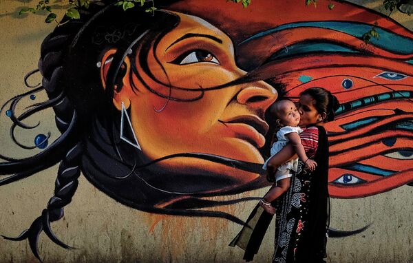 Мама с ребенком проходит мимо граффити в Мумбаи