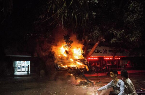 Жители проезжают мимо горящего киоска после акции протеста против строительства химического завода в китайской провинции Гуандун
