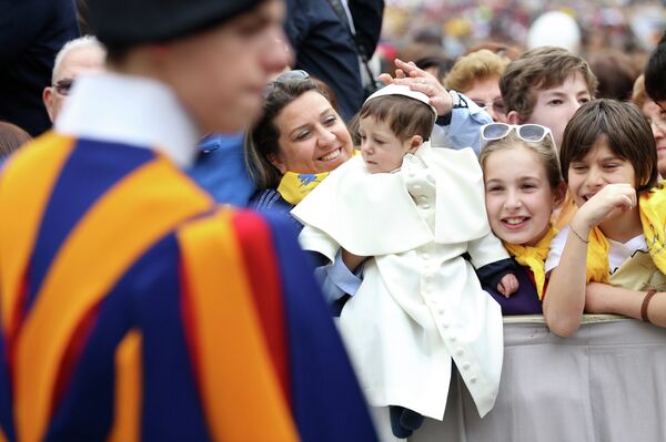 Мать держит ребенка, одетого, как Папа Римский