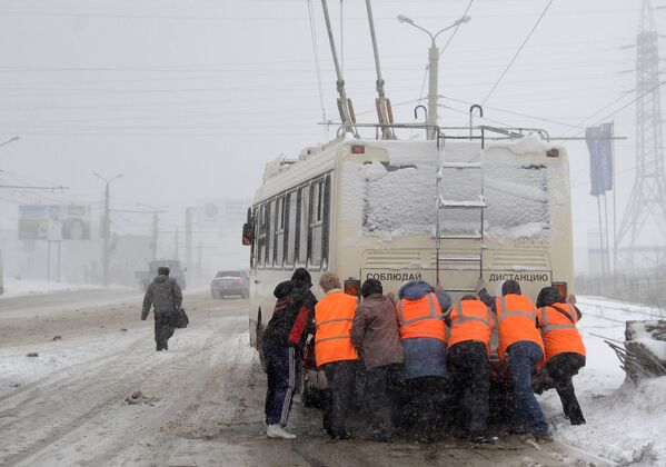 Работники коммунальных служб толкают троллейбус во время сильного снегопада в Челябинске