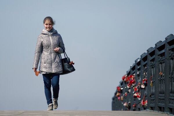 Девушка с ленточкой идет по пешеходному мосту через улицу Нижняя Набережная в Иркутске