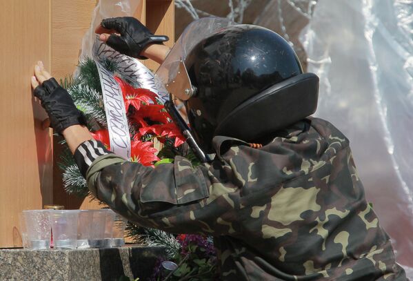 Участник народного ополчения поправляет ленточку на венке в память о жертвах в Одессе перед зданием областной администрации