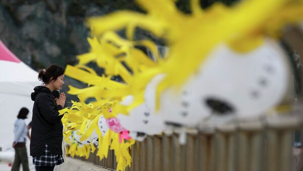 Женщина молится у желтых лент с именами жертв затонувшего парома Севол