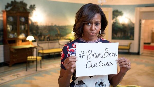 Мишель Обама держит белый лист бумаги, на котором написан хэштег # BringBackOurGirls