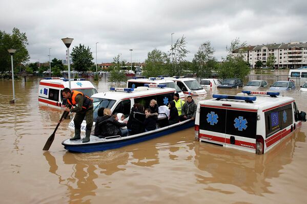 Сербский спасатель направляет лодку между затопленными автомобилями скорой помощи в затопленном городе Оберновац