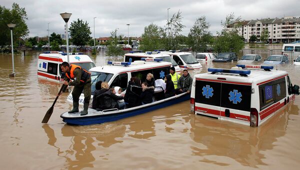 Сербский спасатель направляет лодку между затопленными автомобилями скорой помощи в затопленном городе Оберновац