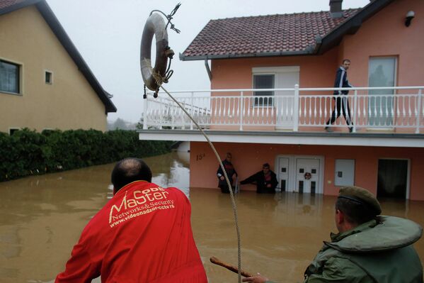 Человек бросает спасательный круг в сторону людей, которые ждут эвакуации из затопленном доме в городе Оберновац