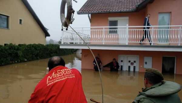 Человек бросает спасательный круг в сторону людей, которые ждут эвакуации из затопленном доме в городе Оберновац