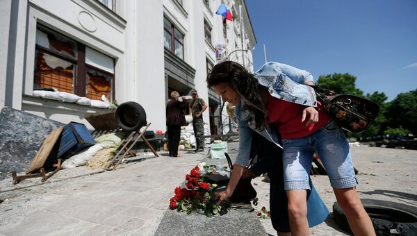 Женщина кладет цветы на место гибели людей у здания обладминистрации в Луганске