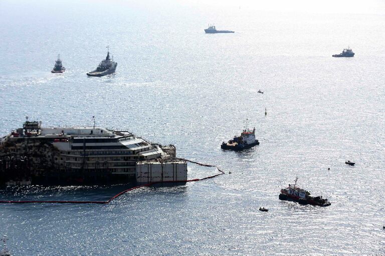 Круизный лайнер Коста Конкордия в окружении буксиров во время перемещения в порт Генуи