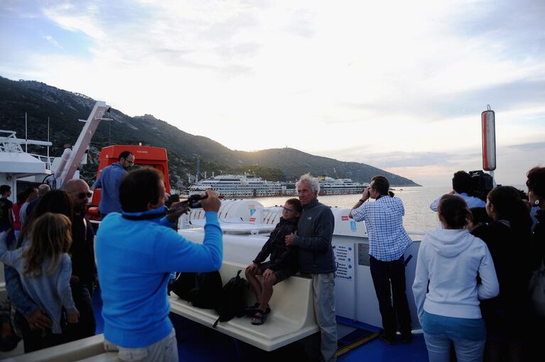 Туристы и журналисты фотографируются на фоне круизного лайнера Коста Конкордия