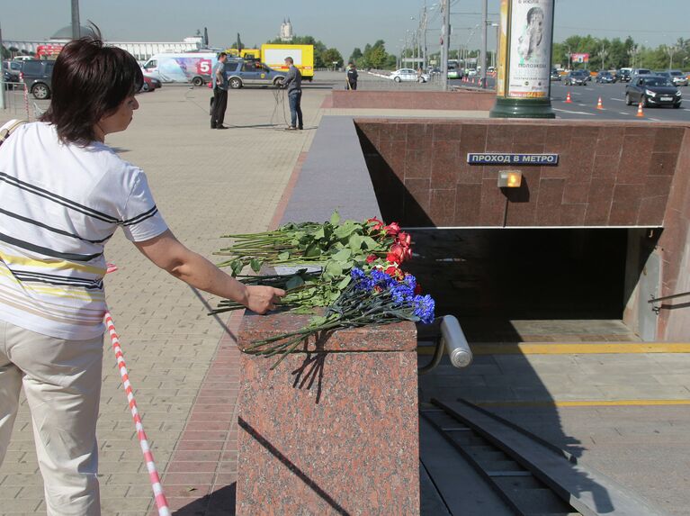 Женщина возлагает цветы у пешеходного перехода станции метро Парк победы