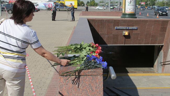 Женщина возлагает цветы у пешеходного перехода станции метро Парк победы