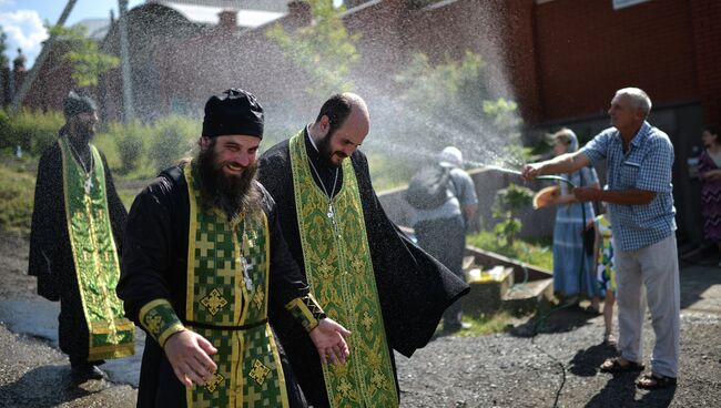 Мужчина поливает водой священнослужителей во время крестного хода