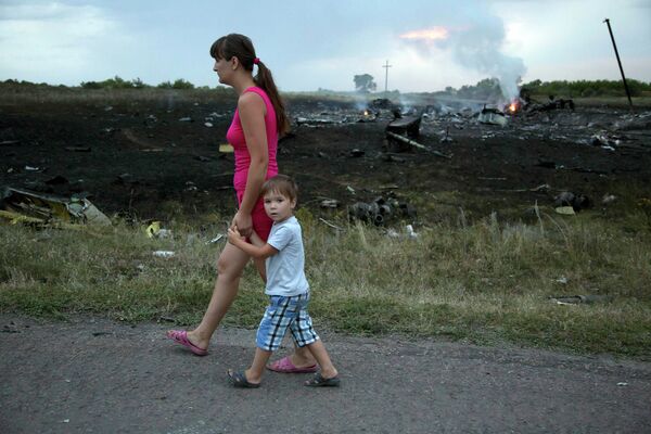 Женщина с ребенком проходят мимо места крушения крушения самолета Боинг 777 в Донецкой области