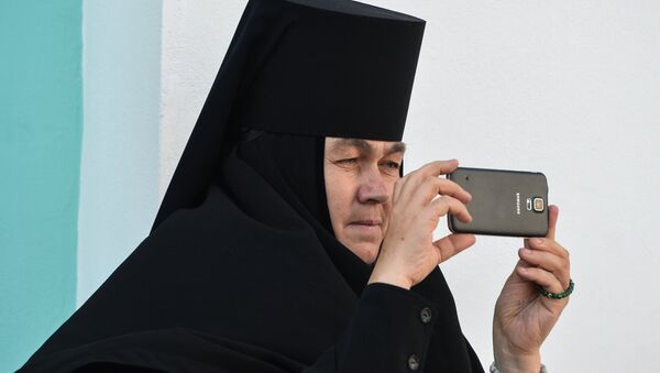 Монахиня фотографирует на мобильный телефон богослужение в Троице-Сергиевой лавре в городе Сергиевом Посаде