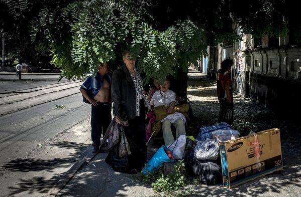 Местные жители сидят под деревом возле своего дома, разрушенного во время артиллерийского обстрела Луганска украинскими силовиками