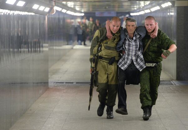 Ополченцы помогают инвалиду во время эвакуации жителей Донецка из зоны боевых действий с украинскими силовиками в районе железнодорожного вокзала