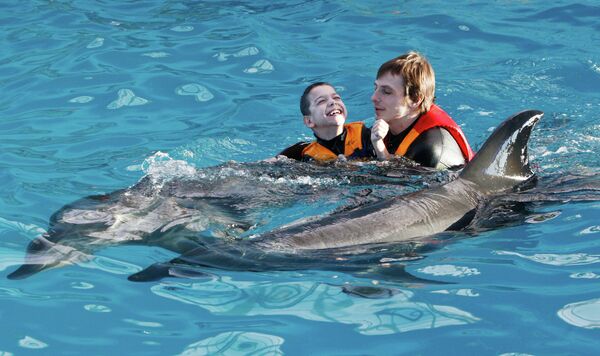 Инструктор занимается с ребенком во время дельфинотерапии в дельфинарии в Минске