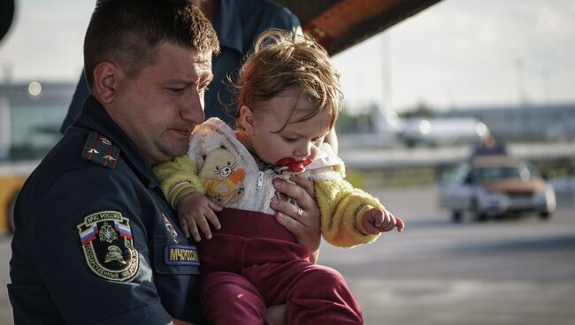 Сотрудник МЧС России несет на руках ребенка из самолета в автобус в аэропорту Санкт-Петербурга