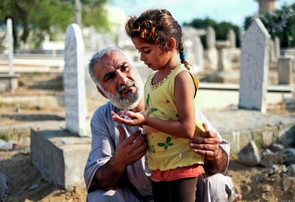 Мужчина с дочкой молятся возле могилы родственников в городе Газа
