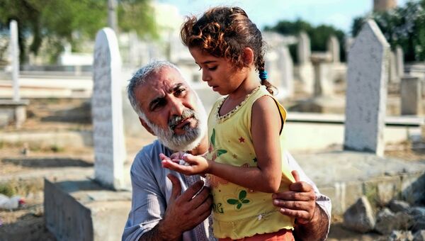 Мужчина с дочкой молятся возле могилы родственников в городе Газа