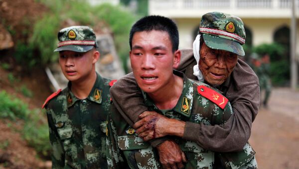 Военный парамедик несет раненого старика в провинции Юньнань, Китай